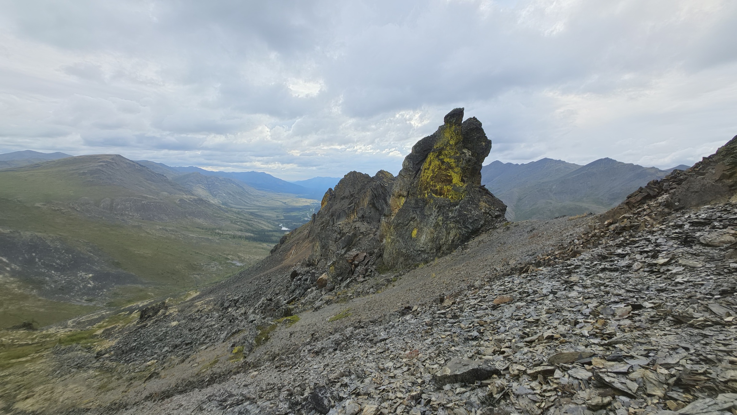 Looking back at the third spire across a ridge of mixed shale, with the main valley and the highway faintly visible beyond.