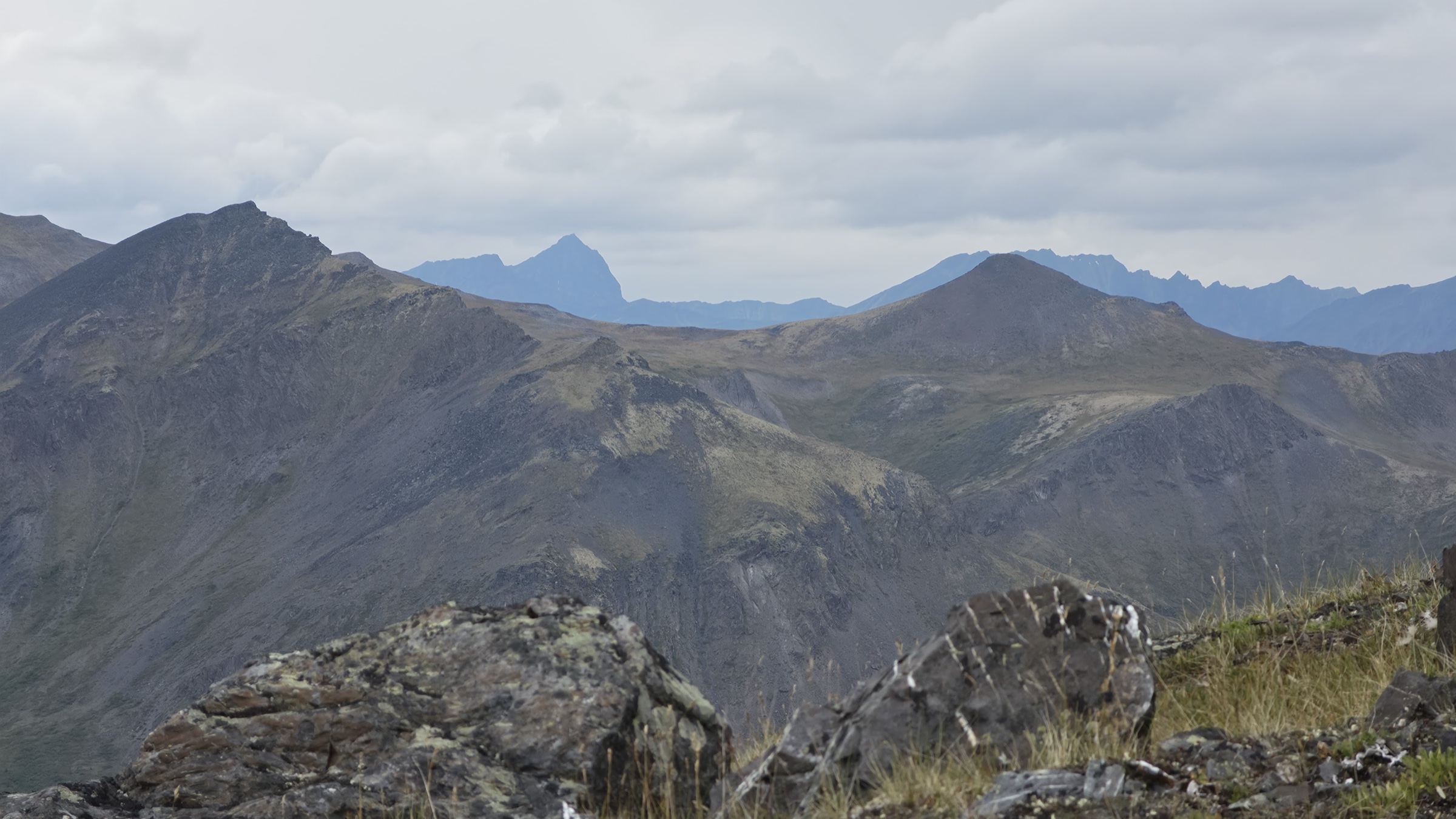 Layered ridges and peaks receding into the distance, with lichen and quartz covered boulders blurred in the foreground.